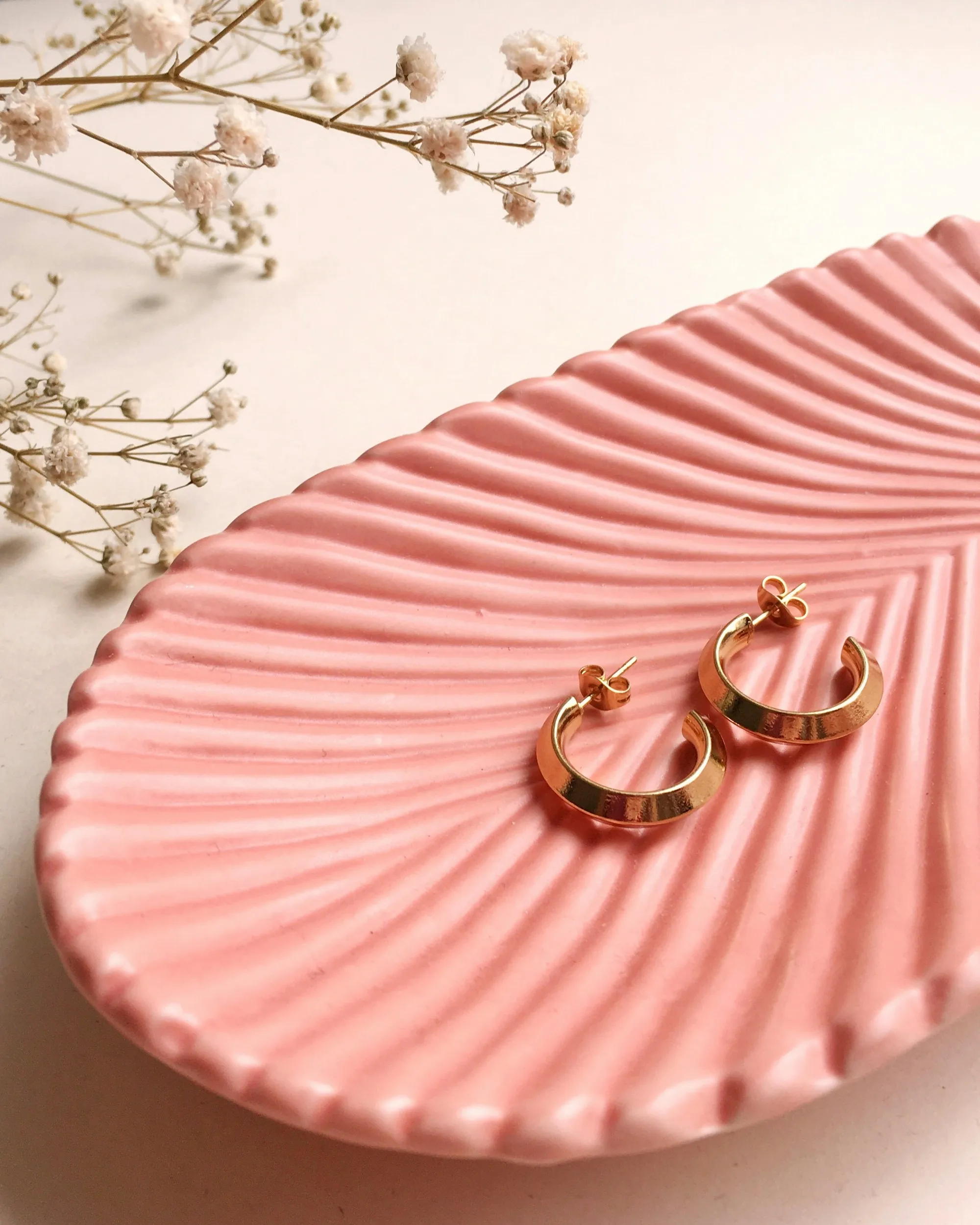 Paire de créoles dorées sur une coupelle rose
